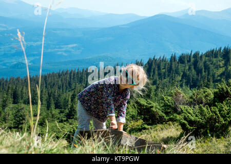 Bambina in occhiali da sole è di graffiare qualcosa sulla pietra. Sullo sfondo le cime delle montagne dei Carpazi Foto Stock