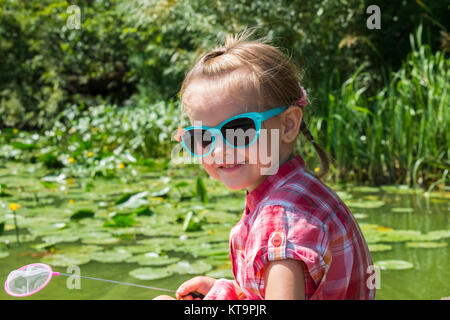 Bambina in bicchieri con un piccolo net nelle sue mani si trova lungo il fiume Foto Stock