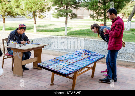 Due visitatori Acquisto di piastrelle dipinte a mano fatte da un artista locale presso il Bibi Khanym moschea, Samarcanda, Uzbekistan Foto Stock