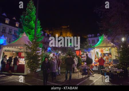 La gente passi oltre il mercato di Natale presso il Kornmarkt Mais (piazza del Mercato) a notte. Il castello di Heidelberg può essere visto in background. La Chris Foto Stock