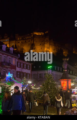 La gente passi oltre il mercato di Natale presso il Kornmarkt Mais (piazza del Mercato) a notte. Il castello di Heidelberg può essere visto in background. La Chris Foto Stock