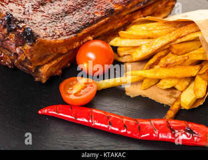 Costolette alla griglia con patate fritte su sfondo nero Foto Stock