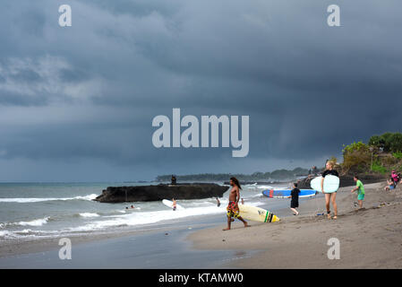 Destinazione di viaggio, scoprire il surf paradise. Surfisti con tavole da surf sulla sabbia vulcanica beach, nuvole di tempesta, cattura le onde. Batu Bolong Beach, CA Foto Stock