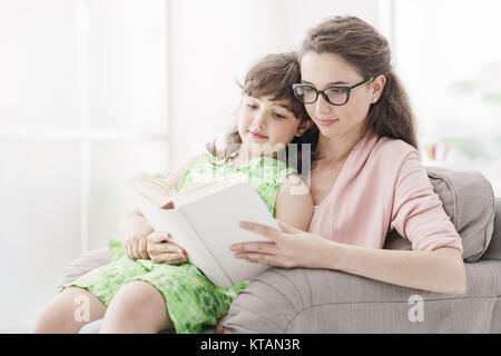 Giovane madre e bambino in un momento di relax a casa nel soggiorno, essi sono seduti sulla poltrona e la lettura di un libro insieme Foto Stock