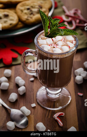 Frech cioccolata calda con bit di candy cane e una manciata di mini marshmallows. Un piatto casereccio biscotti con scaglie di cioccolato è in secondo piano Foto Stock