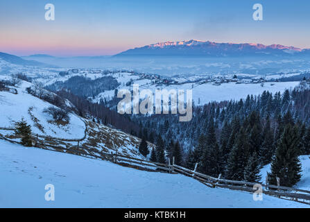 Picturesquet paesaggio rurale con la snowy Rucar-Bran passano nella valle delle montagne di Bucegi al tramonto, Pestera village, Brasov county, Transilvania Foto Stock