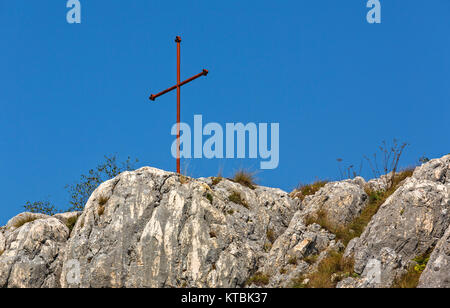 Red croce di ferro sulla cima della montagna rocce, oltre il cielo blu chiaro. Foto Stock