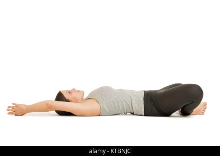 Seitliche Profil-Ganzkörper-Ansicht einer auf dem Rücken liegenden jungen Frau in der Yogaposition 'liegender Schmetterling' (supta baddha konasana) auf weißem Hintergrund. Foto Stock