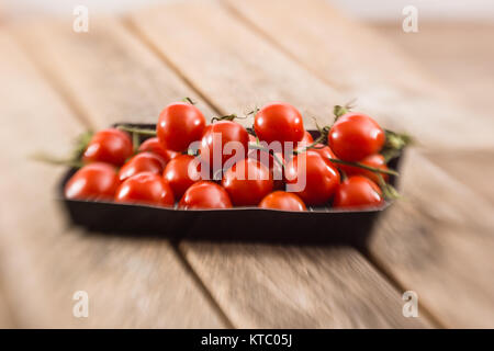 Kleine Rispentomaten in einer Schale auf einem Holzbrett Foto Stock