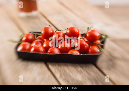 Kleine Rispentomaten in einer Schale auf einem Holzbrett Foto Stock