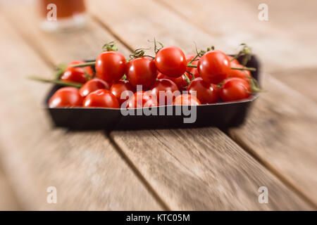 Kleine Rispentomaten in einer Schale auf einem Holzbrett Foto Stock