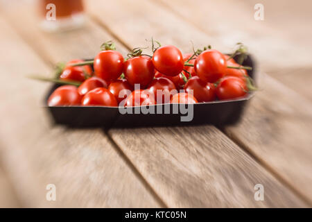 Kleine Rispentomaten in einer Schale auf einem Holzbrett Foto Stock