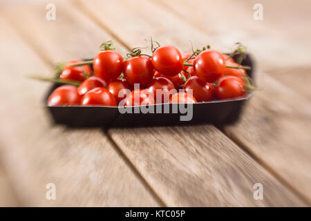 Kleine Rispentomaten in einer Schale auf einem Holzbrett Foto Stock