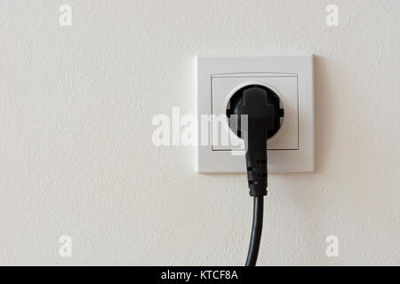 Vicino la foto di un nero 220 volt spina di alimentazione inserito in una presa di corrente con copyspace Foto Stock