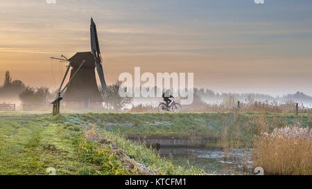 Ciclista nella nebbia di mattina presto con il paesaggio storico Mulino a vento in legno Foto Stock