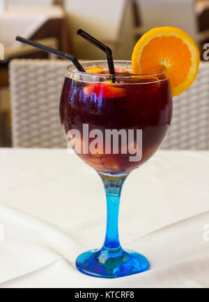 Sangria spagnola servita in un blu di gambi di bicchiere di vino con ghiaccio una fetta di arancio e due cannucce potabile Foto Stock