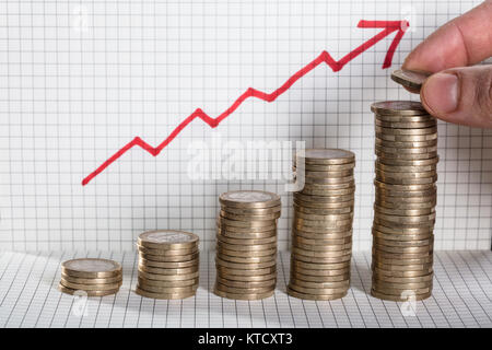 Persona inserimento di moneta sulla moneta impilati con la freccia che mostra il profitto Foto Stock