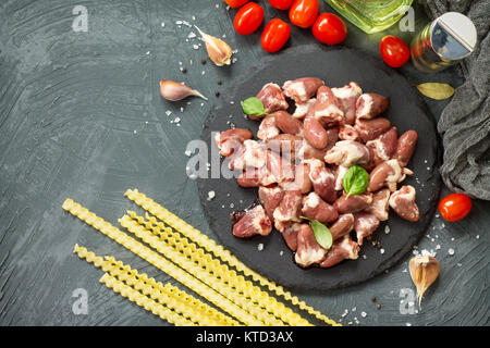 Il pollo crudo carne (fegato cuore), pasta di pomodoro, aglio e spezie al buio su un sfondo di ardesia. Appartamento laico, vista dall'alto con copia spazio. Foto Stock