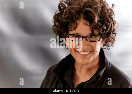 Donna di mezza età con capelli ricci, indossando occhiali guardando sorridente della fotocamera Foto Stock