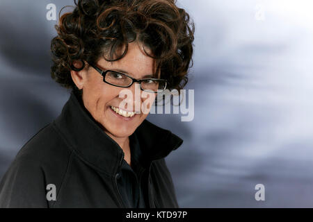 Donna di mezza età con ricci capelli marrone nero che indossa gli occhiali da lettura e sorridente Foto Stock