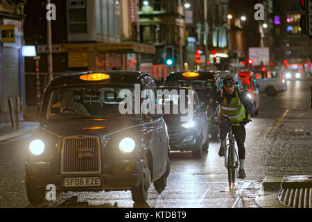 Taxi nero a tarda notte in strada con uomo maschio ciclista sulla bicicletta dando spazio vicino ad altri taxi in una linea di traffico Foto Stock