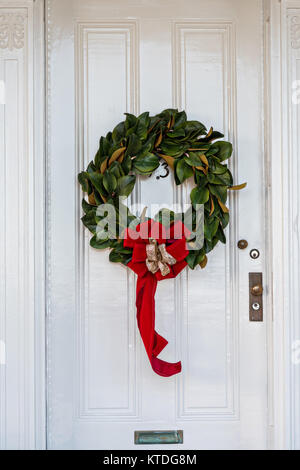 Un basso e tradizionale paese di foglia di Magnolia ghirlanda di Natale pende da una porta di legno su una storica casa lungo King Street a Charleston, Sc. Foto Stock