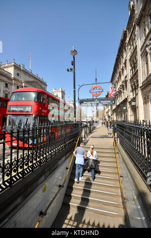 Persone che lasciano la stazione della metropolitana di Westminster con autobus rossi di Londra in Parliament Street. Gradini che si innalzano dalla stazione della metropolitana Foto Stock