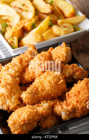 Alette di pollo fritte nel pangrattato e fette di patate close-up su una piastra verticale. Foto Stock
