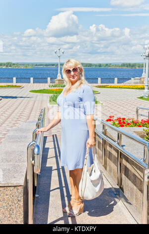 Donna bionda in vestito blu in piedi sul terrapieno Foto Stock