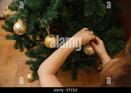 Donna adulta decorare l'albero di natale con una decorazione palla a casa. Foto Stock