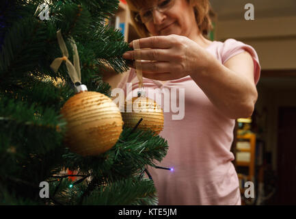 Donna adulta decorare l'albero di natale con una decorazione palla a casa. Foto Stock