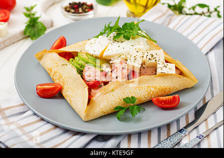 Cucina francese. La prima colazione, pranzo e spuntini. Frittelle con uovo in camicia, il formaggio feta, prosciutto fritto, avocado e pomodori sul tavolo bianco Foto Stock