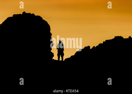 Silhouette di un pescatore in piedi su una formazione di roccia al tramonto dalla piccola spiaggia della Corona, Corona del Mar, California Foto Stock