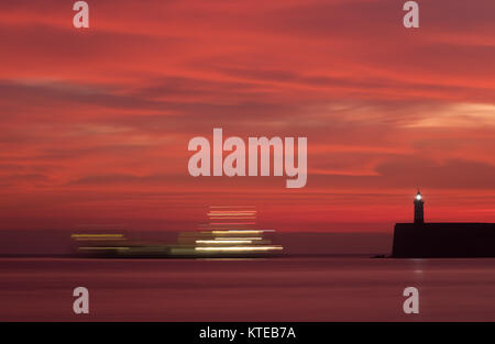 Molto luminose Red Sunset over Newhaven faro, Sussex, Regno Unito, con un movimento di barche da pesca e sentieri di luce, di lasciare il porto. Foto Stock