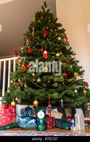 Avvolgere i regali di Natale sotto un albero di Natale in una famiglia la stanza di seduta con un tappeto persiano Foto Stock