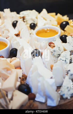 Il piatto di formaggi. Assortimento di formaggi con noci e miele il miele dal bilanciere su legno bianco che serve scheda sopra in calcestruzzo bianco sullo sfondo di texture. Vista da sopra con lo spazio. Tema di antipasti Foto Stock