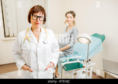 Ritratto di una donna senior ginecologo in piedi in ufficio con paziente sullo sfondo Foto Stock