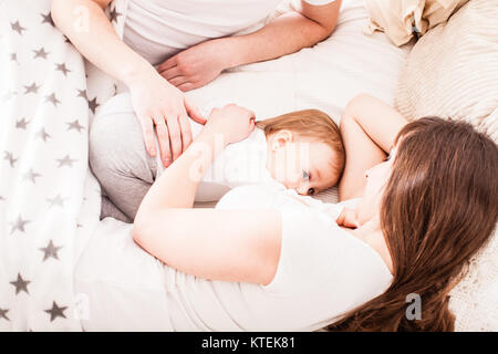 La famiglia felice sul letto. Madre e più lontano il sonno con la loro bambina. La mamma è allattare al seno il suo bambino figlia Foto Stock