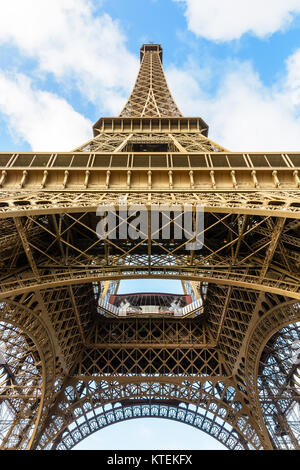 Vista dal basso della Torre Eiffel che mostra la sua lacy struttura metallica e di colore marrone sotto un cielo blu con nuvole bianche. Foto Stock