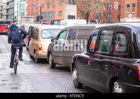 Ciclista uomo sulla bicicletta pedalando passato una fila di London Black Cab taxi su Holborn, Londra, Regno Unito Foto Stock