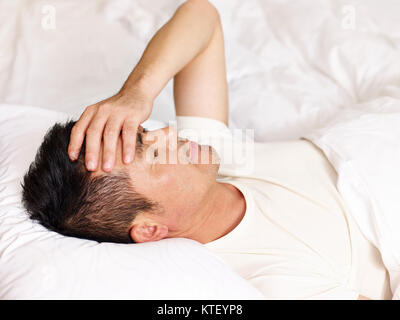 Uomo asiatico giacente sul retro nel letto mano sulla fronte. Foto Stock