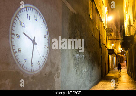 Lone Donna che cammina su un vicolo buio e la proiezione del grande orologio su una parete vuota. Città vecchia di Viveiro, provincia di Lugo, Galizia, Spagna, Europa Foto Stock