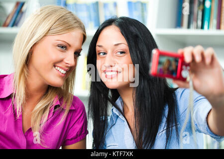Due ragazze degli studenti tenendo selfie nella libreria Foto Stock