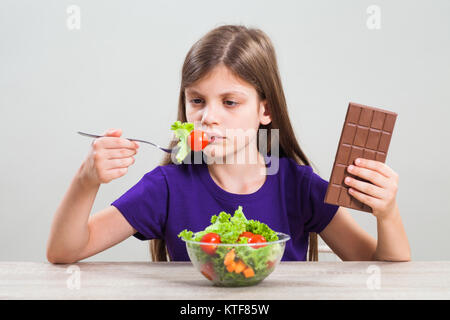 Bambina è infelice perché non le piace mangiare insalata. Lei preferisce il cioccolato. Foto Stock