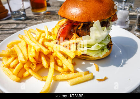 Obesità: tipico pub britannico cibo: un beefburger in un panino con il formaggio e la pancetta e una pila di golden patatine fritte, hamburger e patatine su una piastra bianca Foto Stock