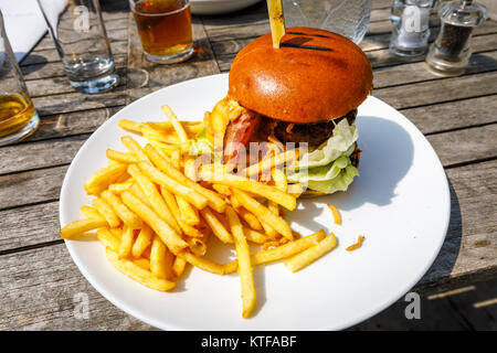 Obesità: tipico pub britannico cibo: un beefburger in un panino con il formaggio e la pancetta e una pila di golden patatine fritte, hamburger e patatine su una piastra bianca Foto Stock