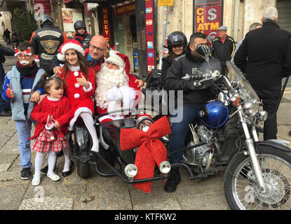 Gerusalemme, Israele. 24 dicembre, 2017. Un uomo vestito da Santa, chi guida come un passeggero in una motocicletta in corrispondenza della testa di una tradizionale processione di Natale, ha la sua fotografia scattata da turisti nella città vecchia di Gerusalemme, 24 dicembre 2017. Foto: Sara Lemel/dpa Credito: dpa picture alliance/Alamy Live News Foto Stock