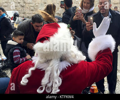 Gerusalemme, Israele. 24 dicembre, 2017. Un uomo vestito da Santa, chi guida come un passeggero in una motocicletta in corrispondenza della testa di una tradizionale processione di Natale, ha la sua fotografia scattata da turisti nella città vecchia di Gerusalemme, 24 dicembre 2017. Foto: Sara Lemel/dpa Credito: dpa picture alliance/Alamy Live News Foto Stock