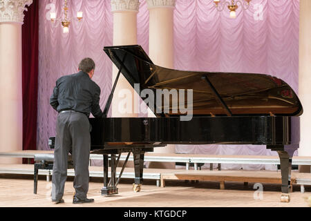 Un uomo in nero si sintonizza un nero pianoforte Foto Stock