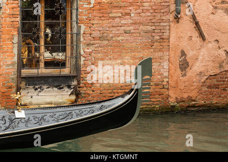 Prua di un iconico gondola sul Canal vela passato una finestra di un edificio in mattoni Foto Stock